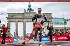 Sebastian Sawe crosses the finish line of the GENERALI BERLIN HALF MARATHON, with the Brandenburg Gate in the background