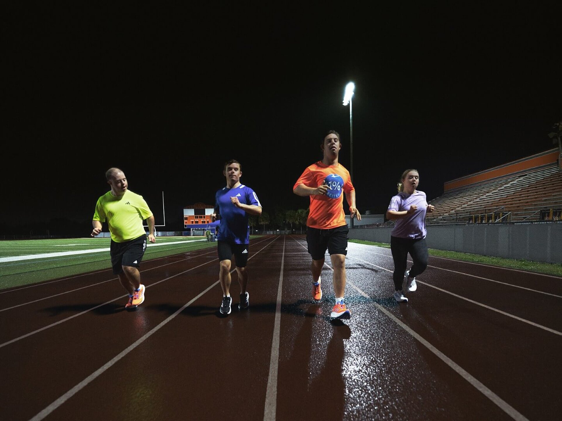 Vier Athleth:innen mit Down-Syndrom laufen in adidas-Kleidung bei Nacht über eine beleuchtete Rennbahn.