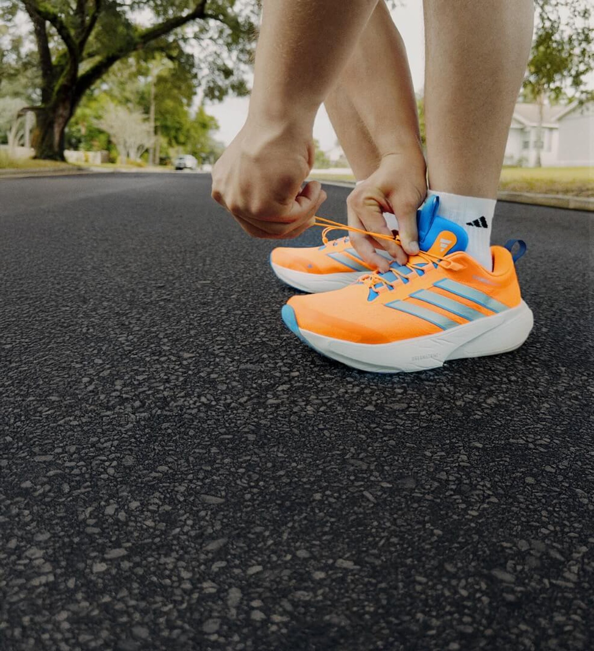 Orangener adidas Supernnova-Schuh mit blauen Akzenten wird auf Asphaltstraße geschnürt.