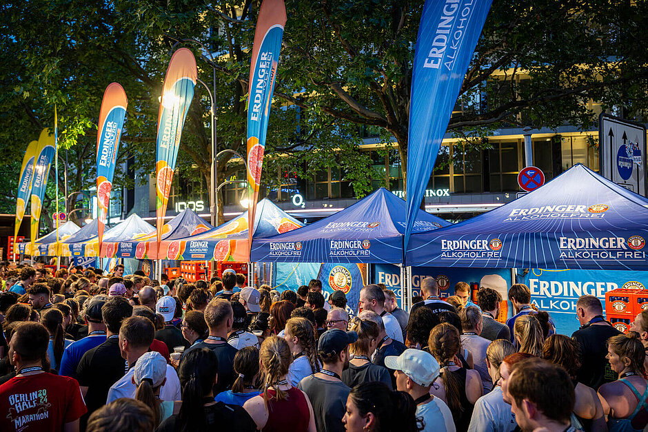 A row of Erdinger Alkoholfrei booths at dusk. A large crowd in front of them.
