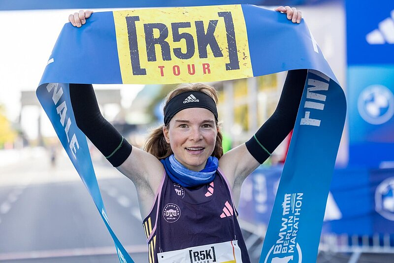 Läuferin des r5k hält Zielband mit Aufdruck des r5k-Logos über ihren Kopf.