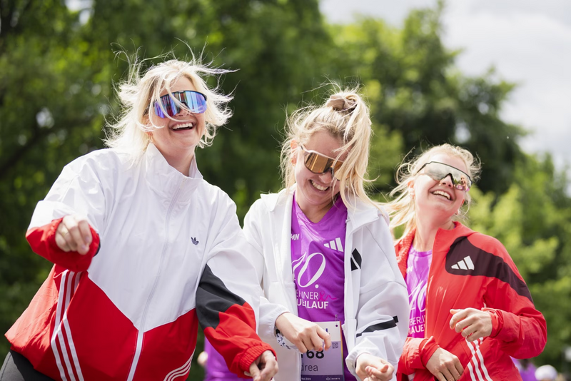 Drei lachende Frauen mit Sonnenbrillen beim VITAMIN WELL Frauenlauf Berlin.
