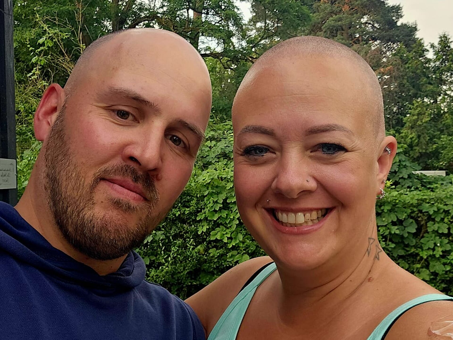 Anja und ihr Freund, beide mit Glatze, lächeln in die Kamera.